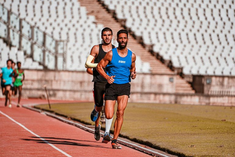 Focused male runners competing on a sports track during a daytime race in a stadium setting.