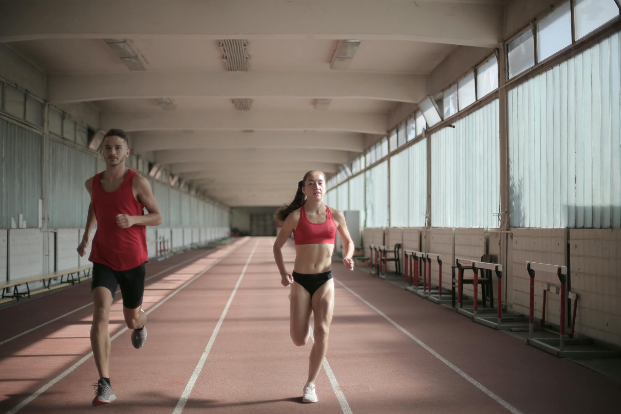 Male and female athletes running on an indoor track, showcasing fitness and energy.