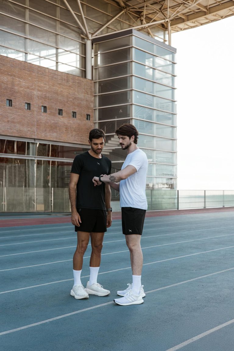 Two male athletes in sportswear discussing a workout strategy on a running track outdoors.