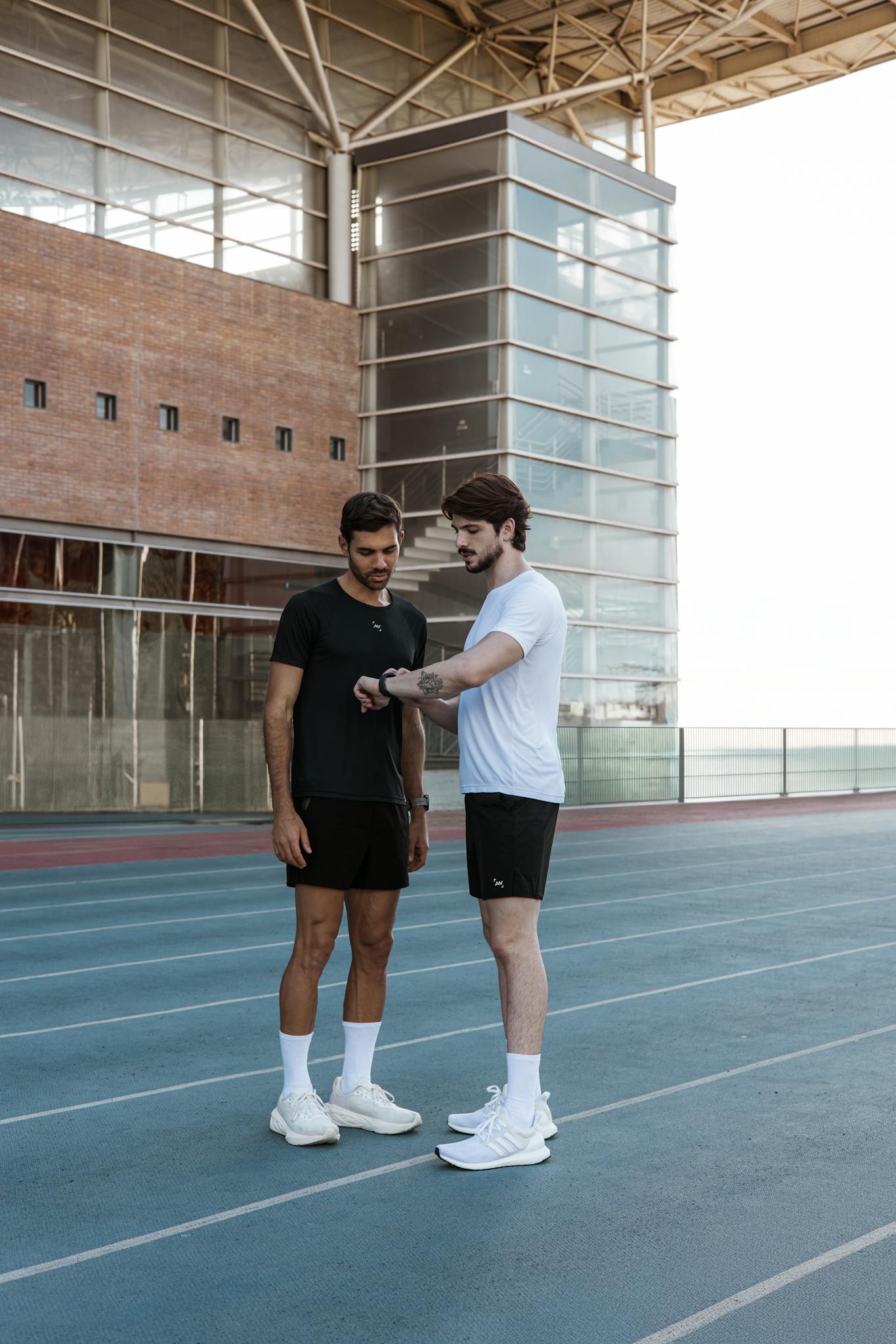 Two male athletes in sportswear discussing a workout strategy on a running track outdoors.